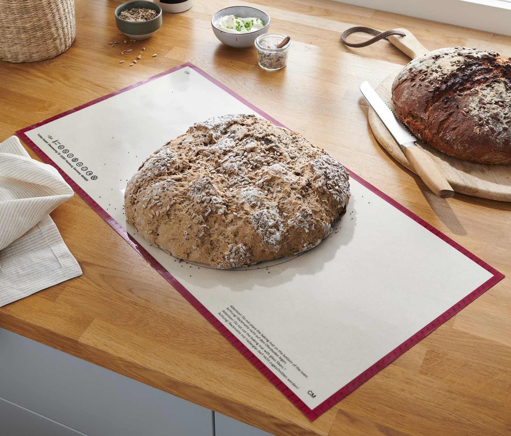 Bochník chleba leží na XL profesionální pečicí podložce na opakované použití na dřevěné desce.