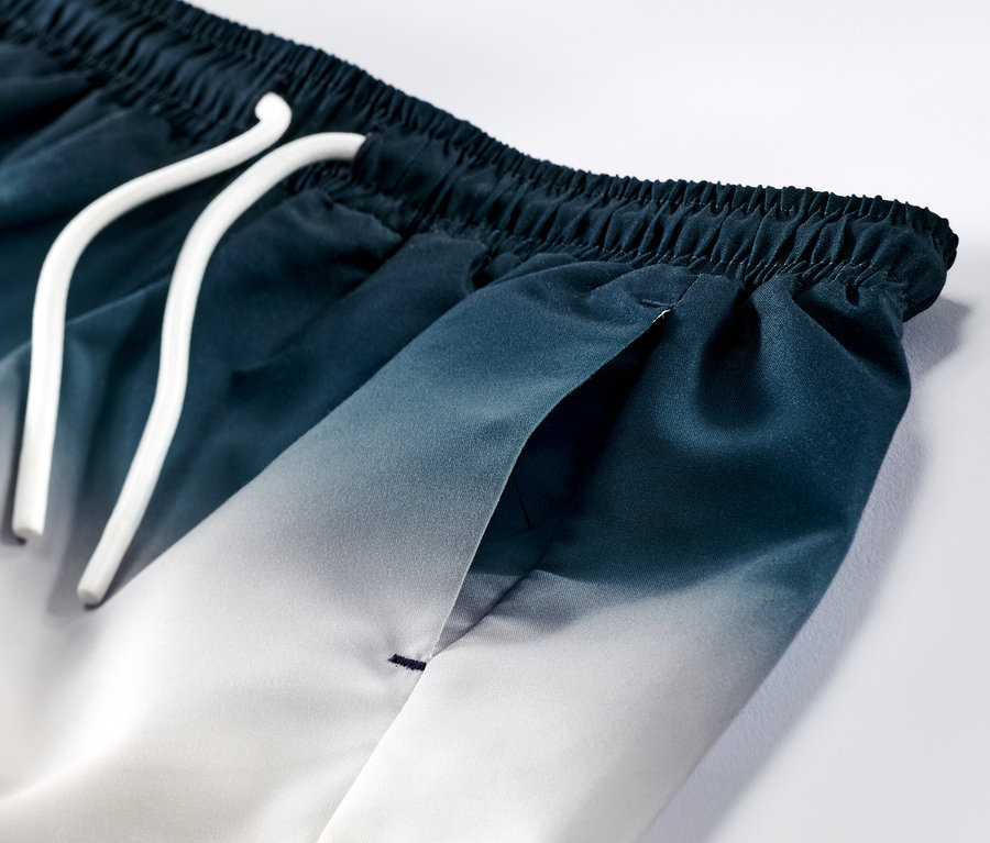 Detail dětských koupacích šortek s modro-bílým gradientem a bílou šňůrkou.