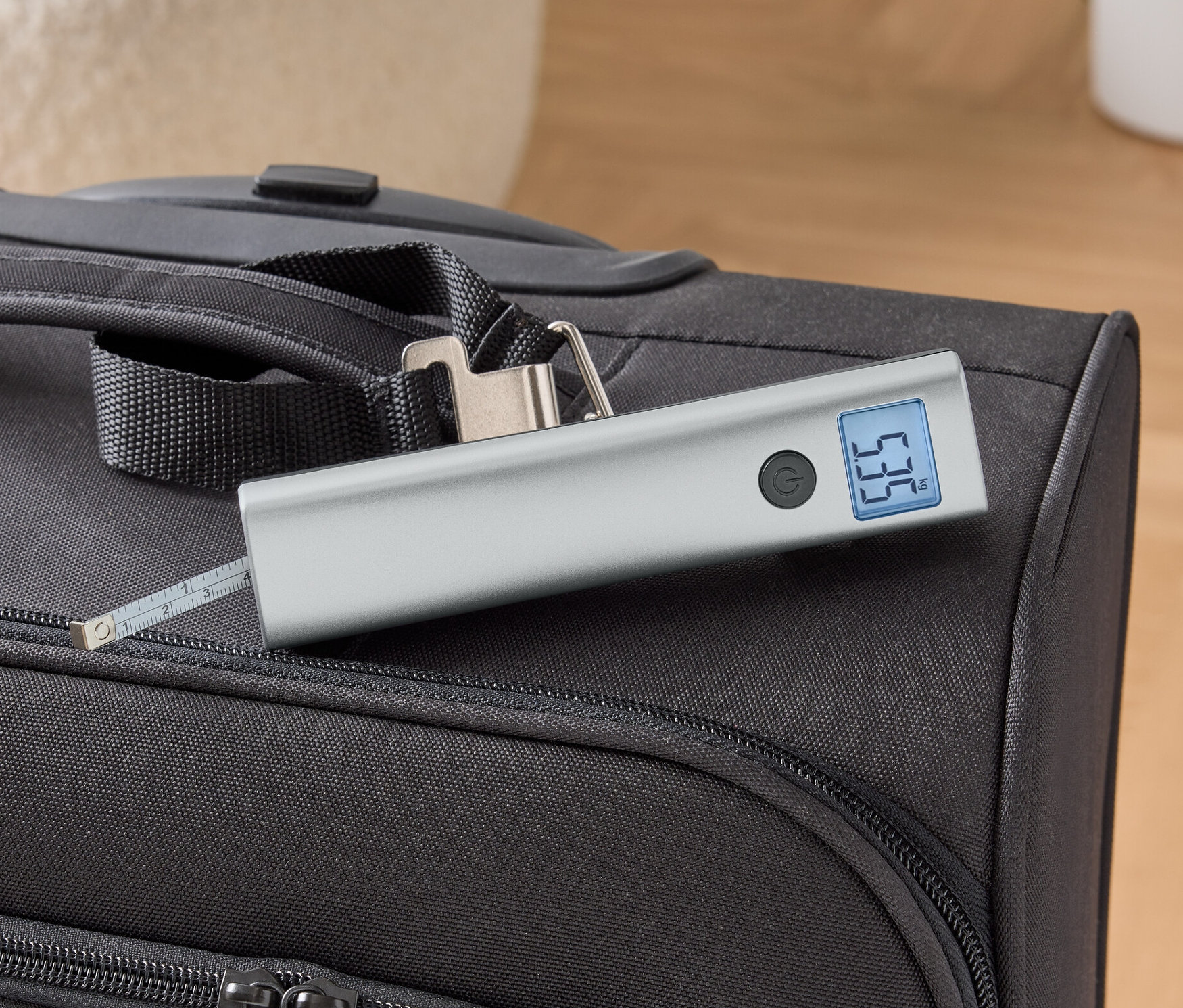 Digitální váha na kufry leží na černém kufru.