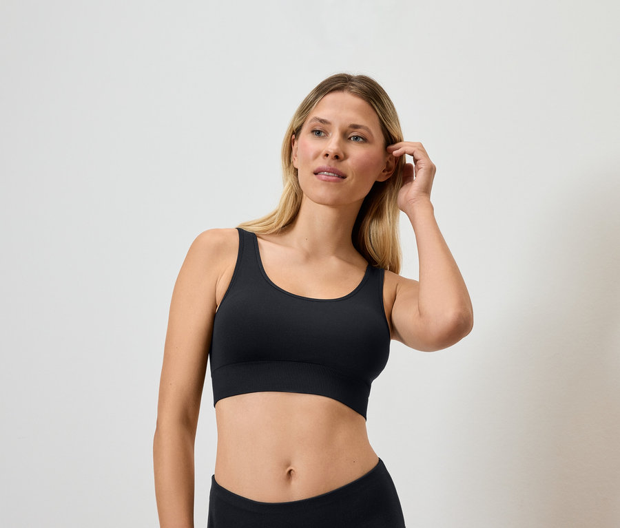 Blondýna v černé sportovní podprsence se dotýká vlasů.