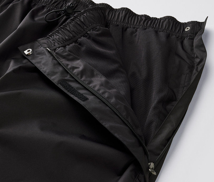 Detailní pohled na černé high-tech kalhoty do deště s rozepnutým zipem a viditelnou síťovanou podšívkou.