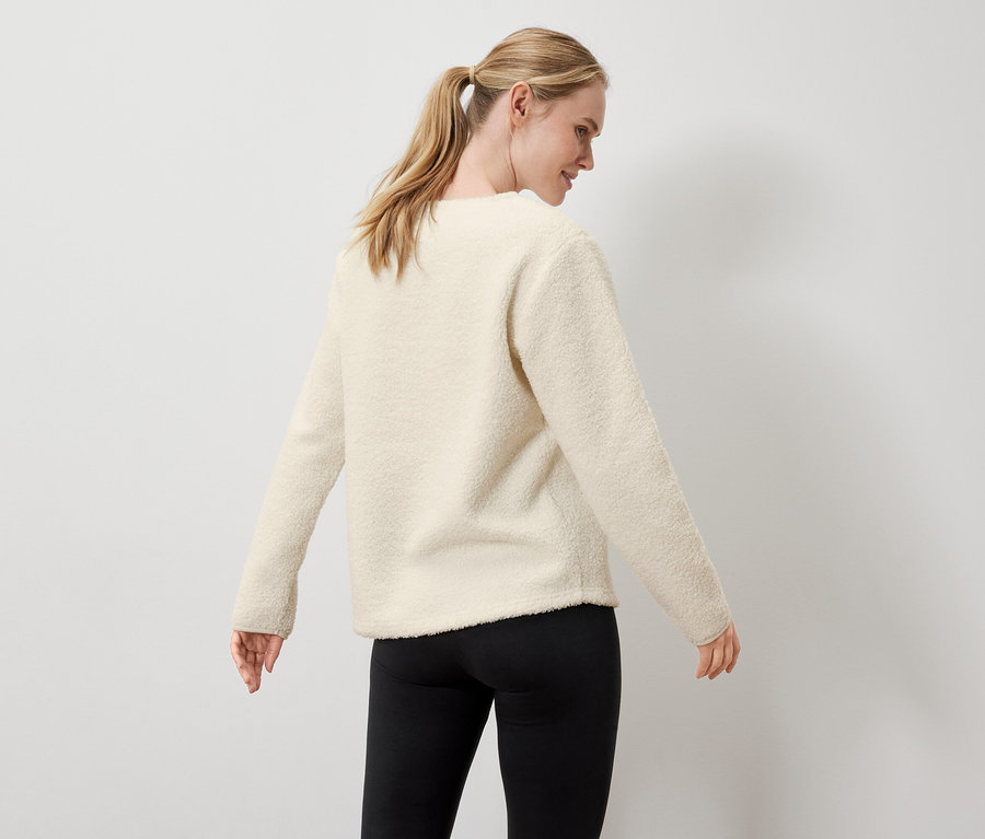 Žena má na sobě krémový svetr a černé legíny.