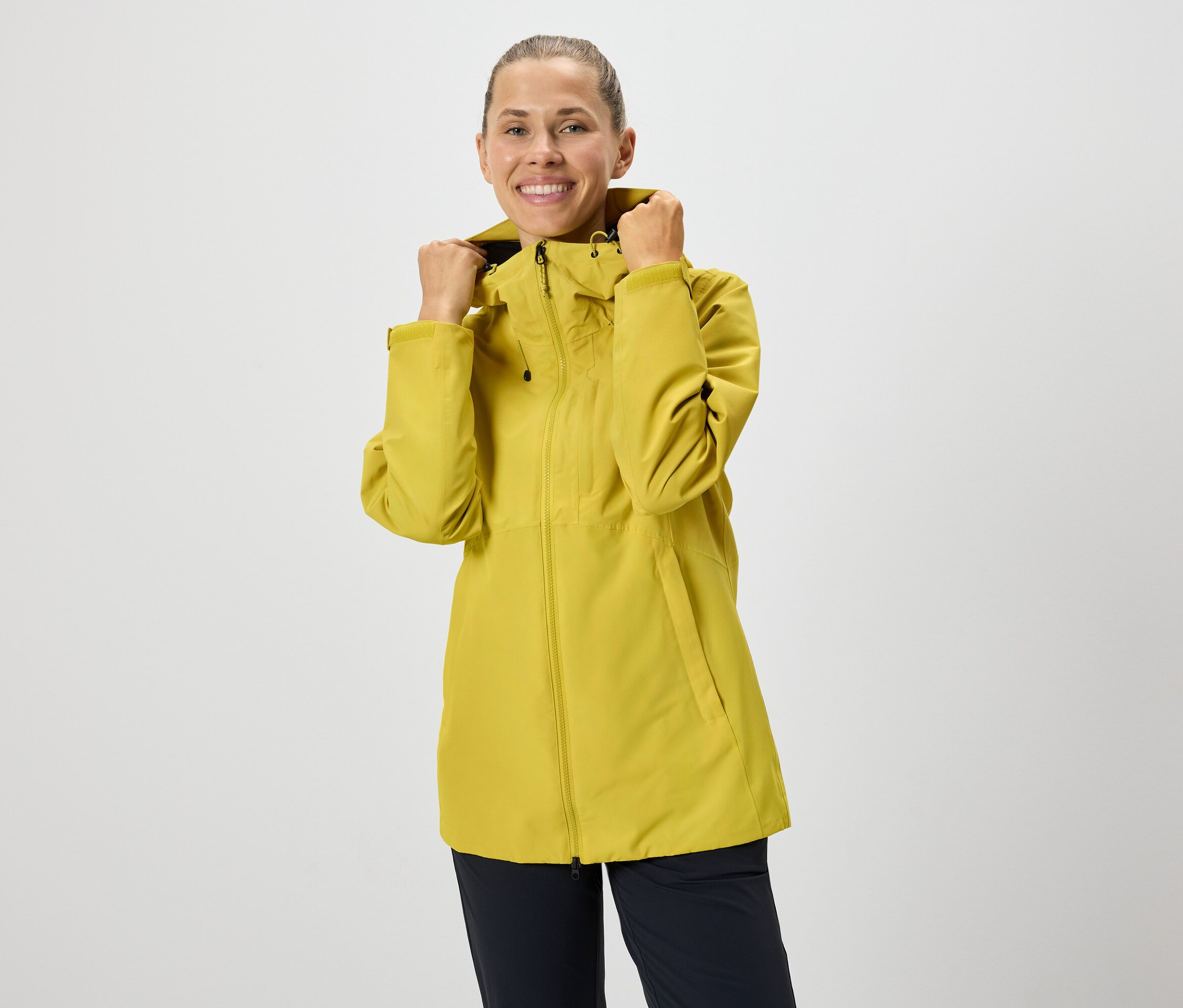 Žena si upravuje kapuci žluté bundy na zip.