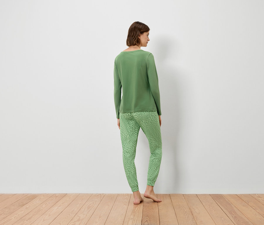 Žena stojí zády k fotoaparátu a má na sobě zelený svetr a zelené kalhoty.