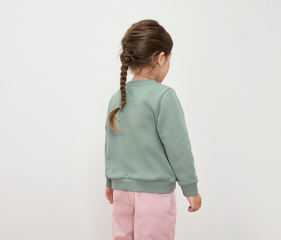 Zezadu pohled na dívku s copem, oblečenou do zelené mikiny a růžových kalhot.