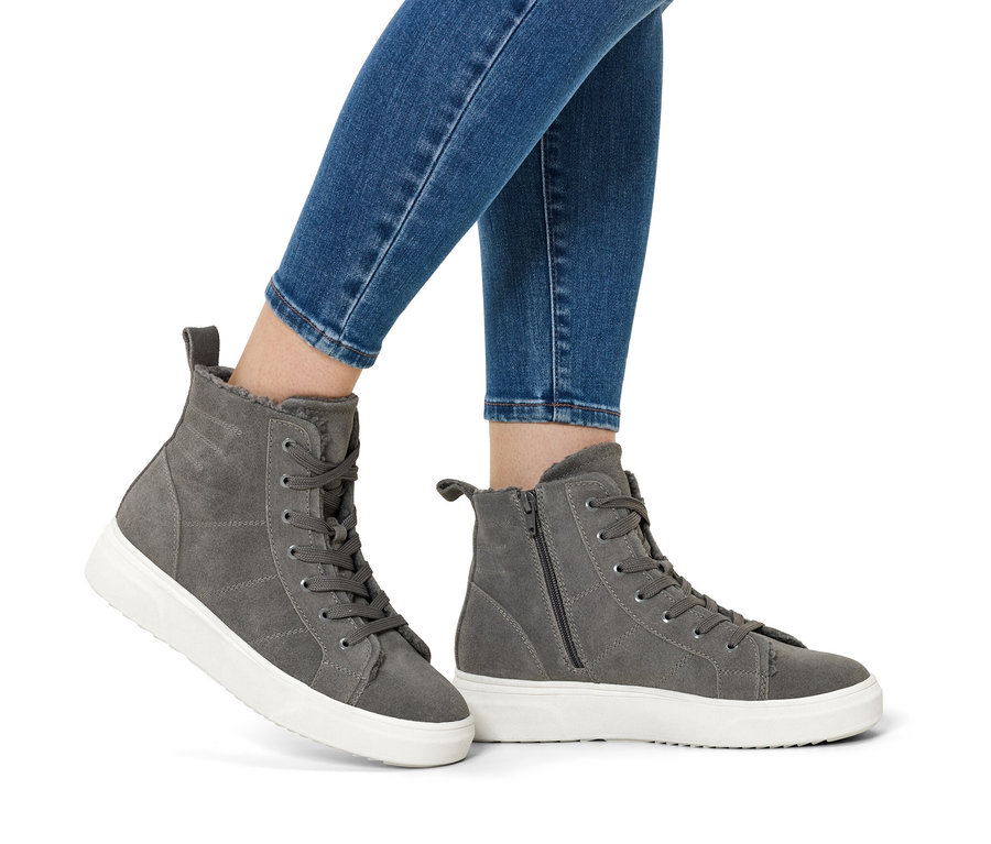 Nohy v modrých džínách a šedých semišových botách na bílé podrážce.