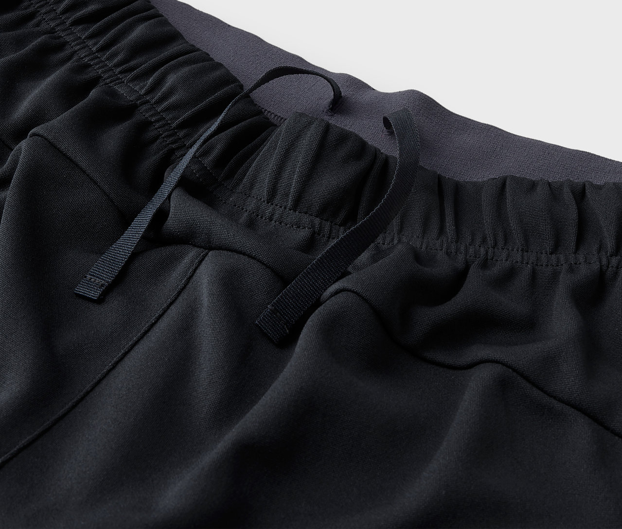 Detail černých sportovních kalhot se stahovací šňůrkou v pase.