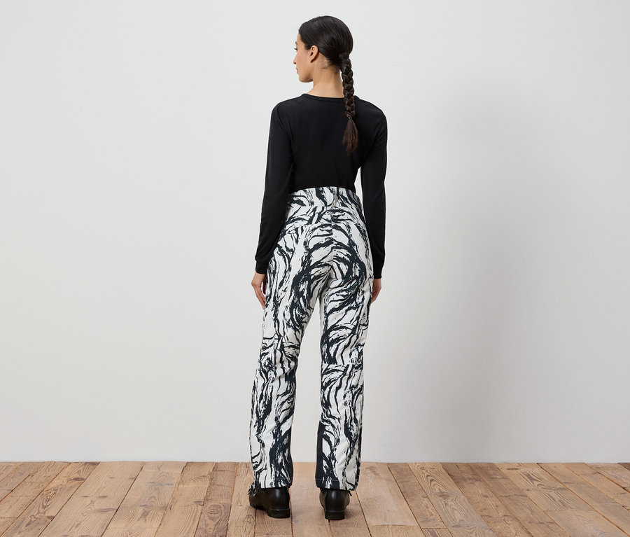 Žena zády k fotoaparátu má na sobě černé tričko s dlouhým rukávem a bílo-černé vzorované kalhoty.