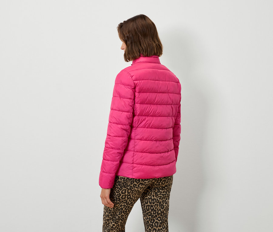 Žena zády k fotoaparátu má na sobě růžovou péřovou bundu a leopardí kalhoty.