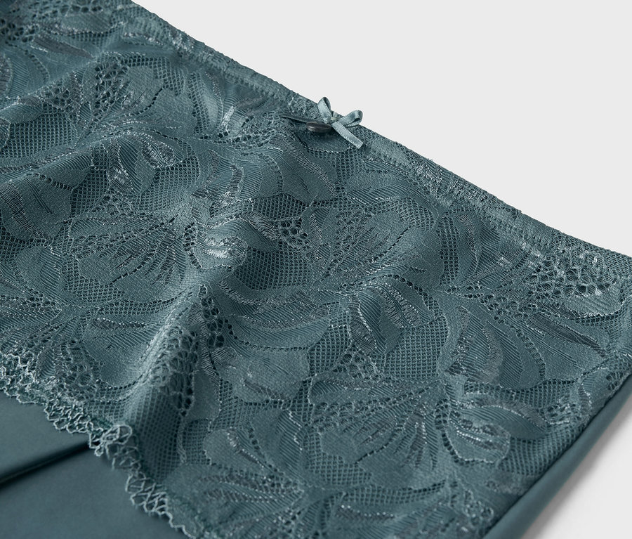 Detailní záběr na modrozelenou krajku s mašličkou v horní části.