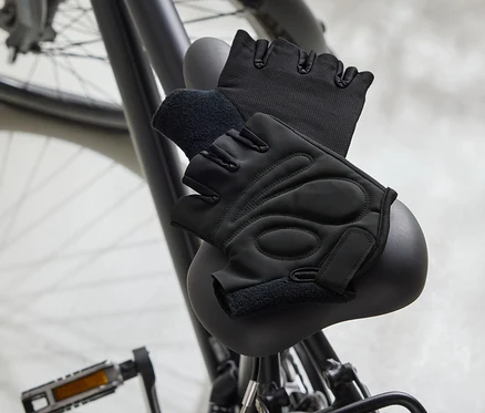 Dvě černé cyklistické rukavice leží na černém sedle kola.