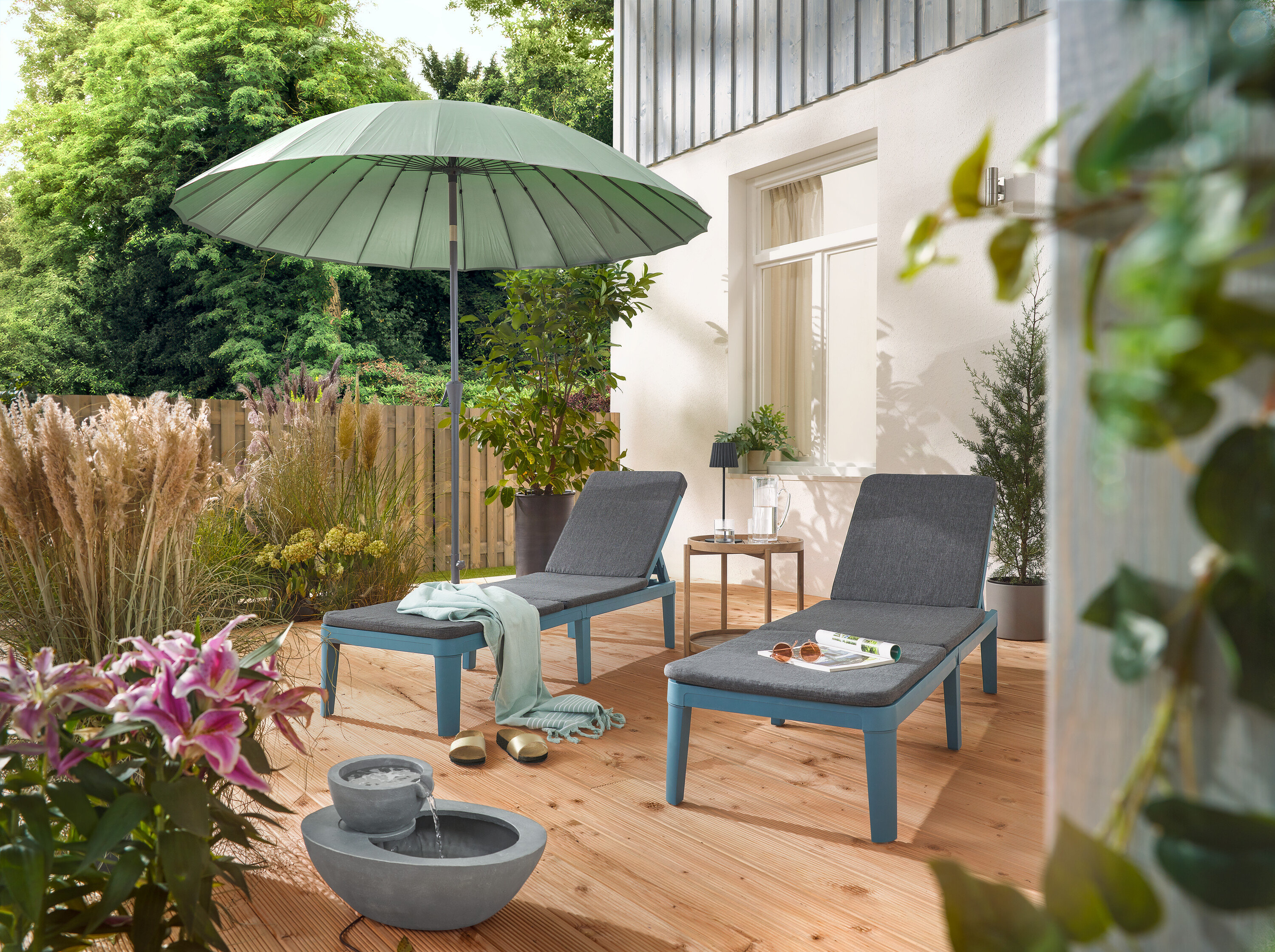 Na terase jsou dvě lehátka pod světle šedým slunečníkem Leco Shanghai a vedle solární zahradní fontány.