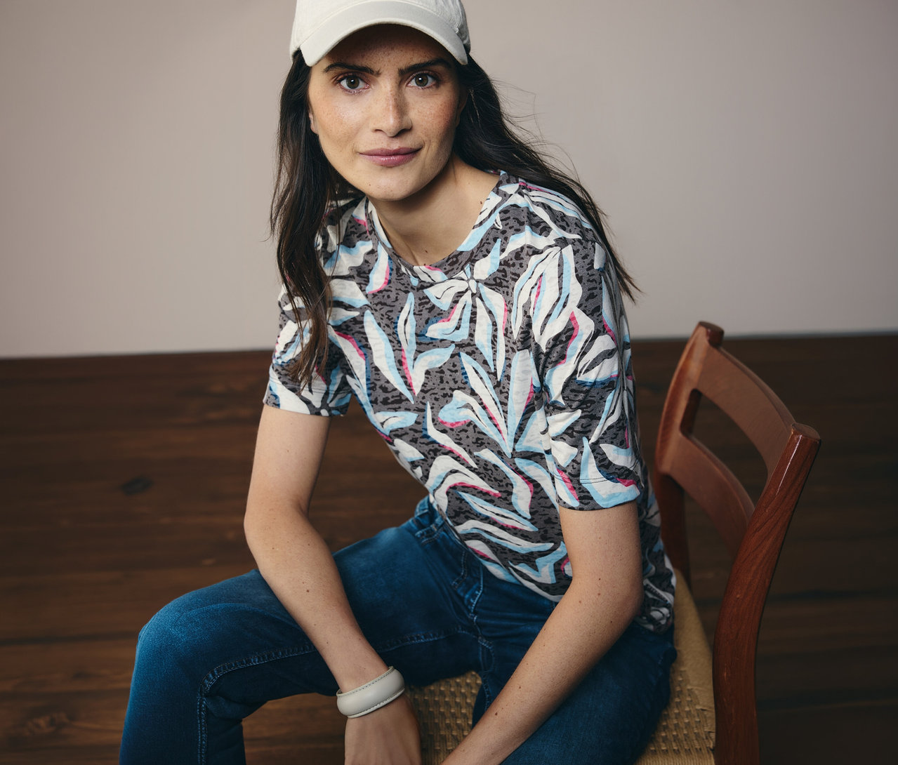 Žena v bílé čepici sedí a má na sobě modré tričko s krátkým rukávem CECIL se vzorem.