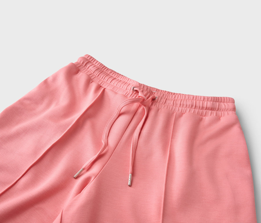 Detailní záběr na korálové kalhoty se stahovací šňůrkou.