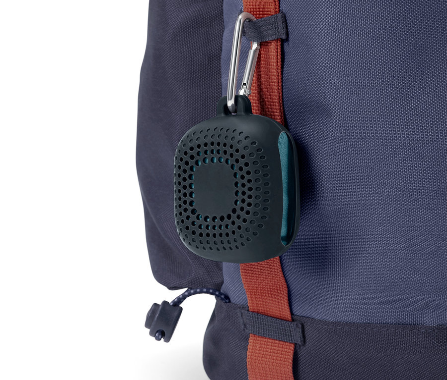 Černé, kulaté pouzdro s otvory visí na karabině z modrého batohu.