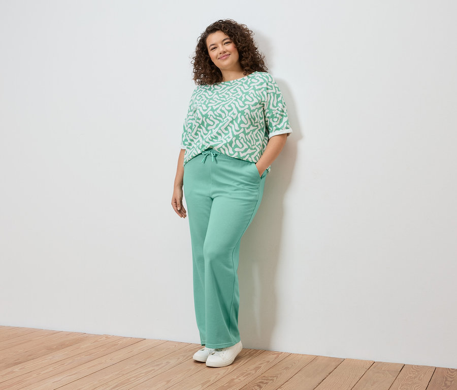 Žena pózuje u zdi, má na sobě světle zelený vzorovaný top, světle zelené kalhoty a bílé tenisky.