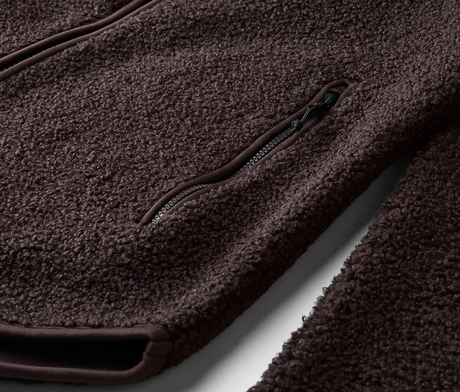 Detail hnědé fleecové bundy se zipem a kapsou na zip.