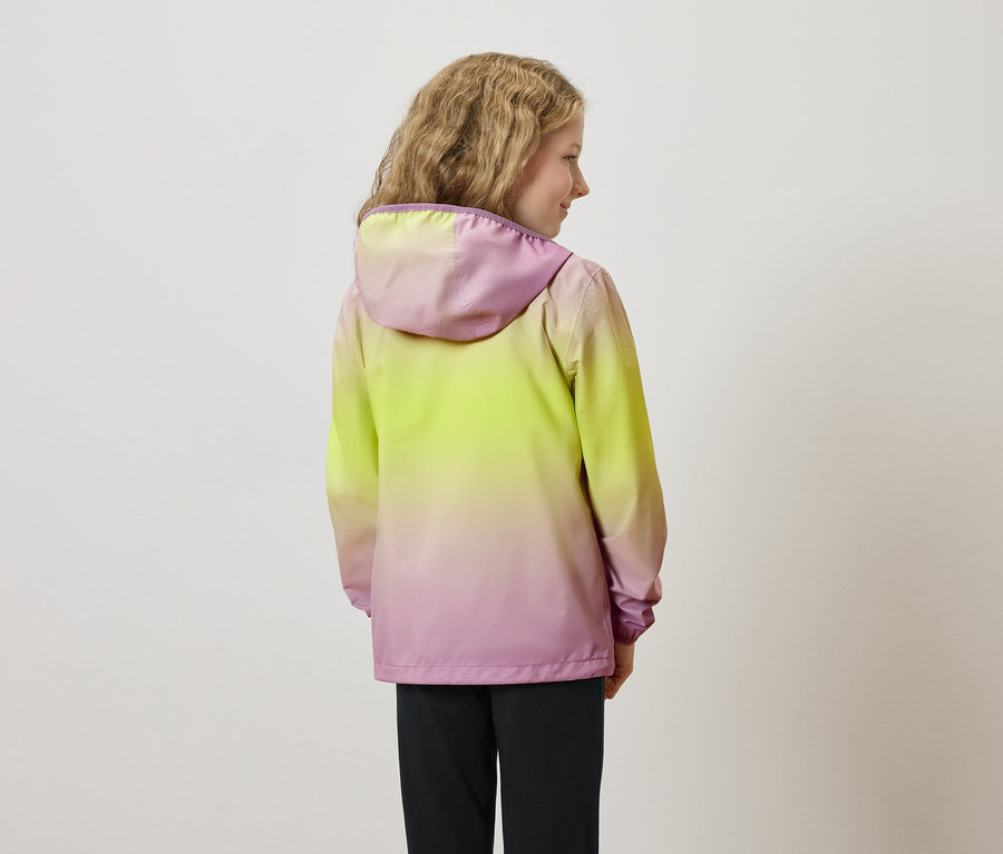 Pohled zezadu na mladou dívku s vlnitými vlasy, oblečenou do žluto-růžové bundy s kapucí a černých kalhot.