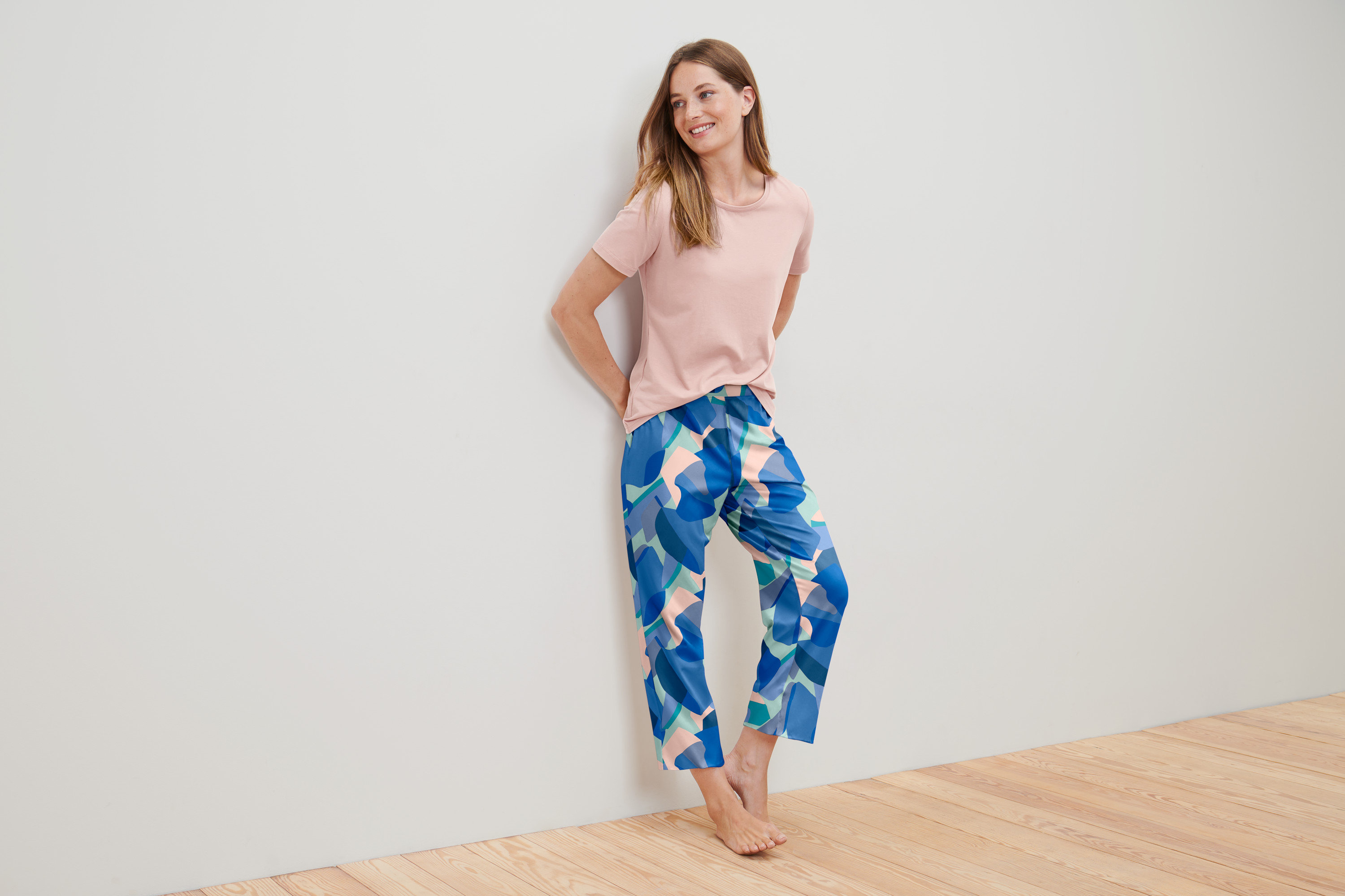 Žena v pyžamu se opírá o stěnu.