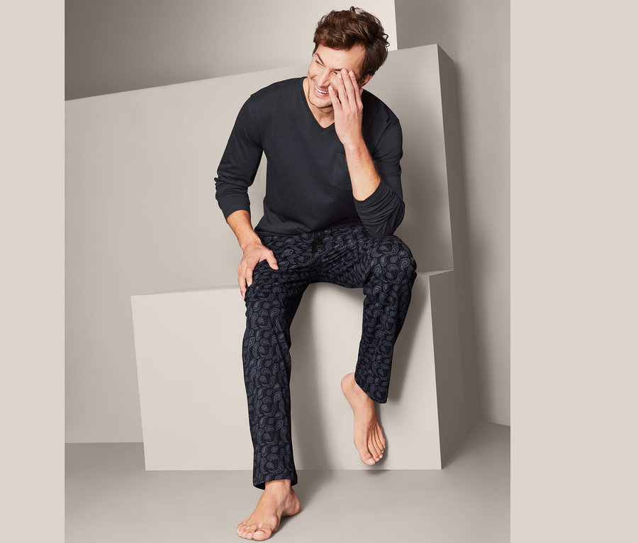 Muž sedí a směje se, má na sobě pyžamo.