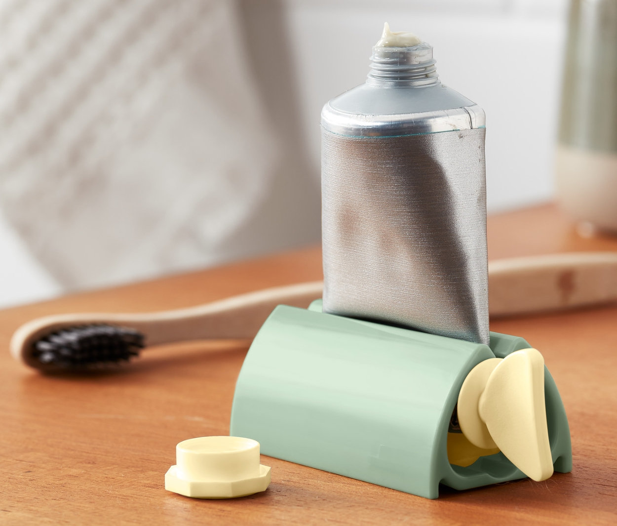 Stříbrná tuba v zeleném vytlačovači tub na dřevěné poličce.