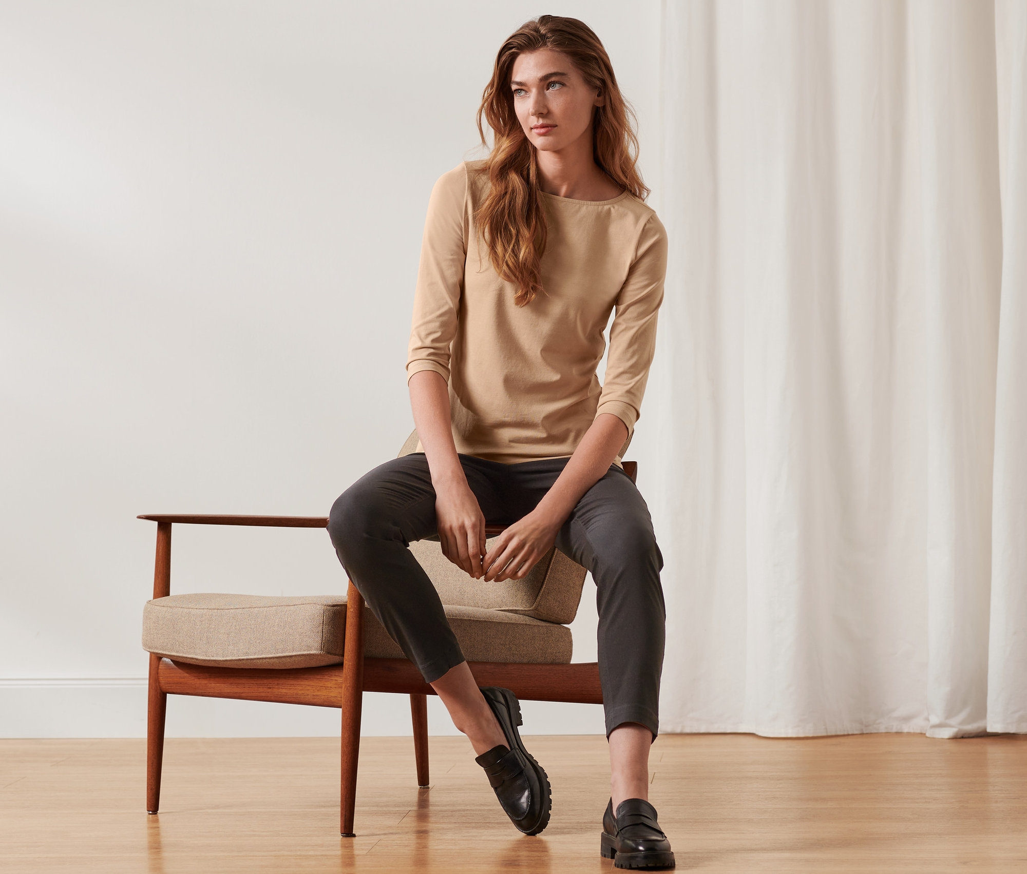 Žena sedí na židli a má na sobě béžové tričko s tříčtvrtečním rukávem.