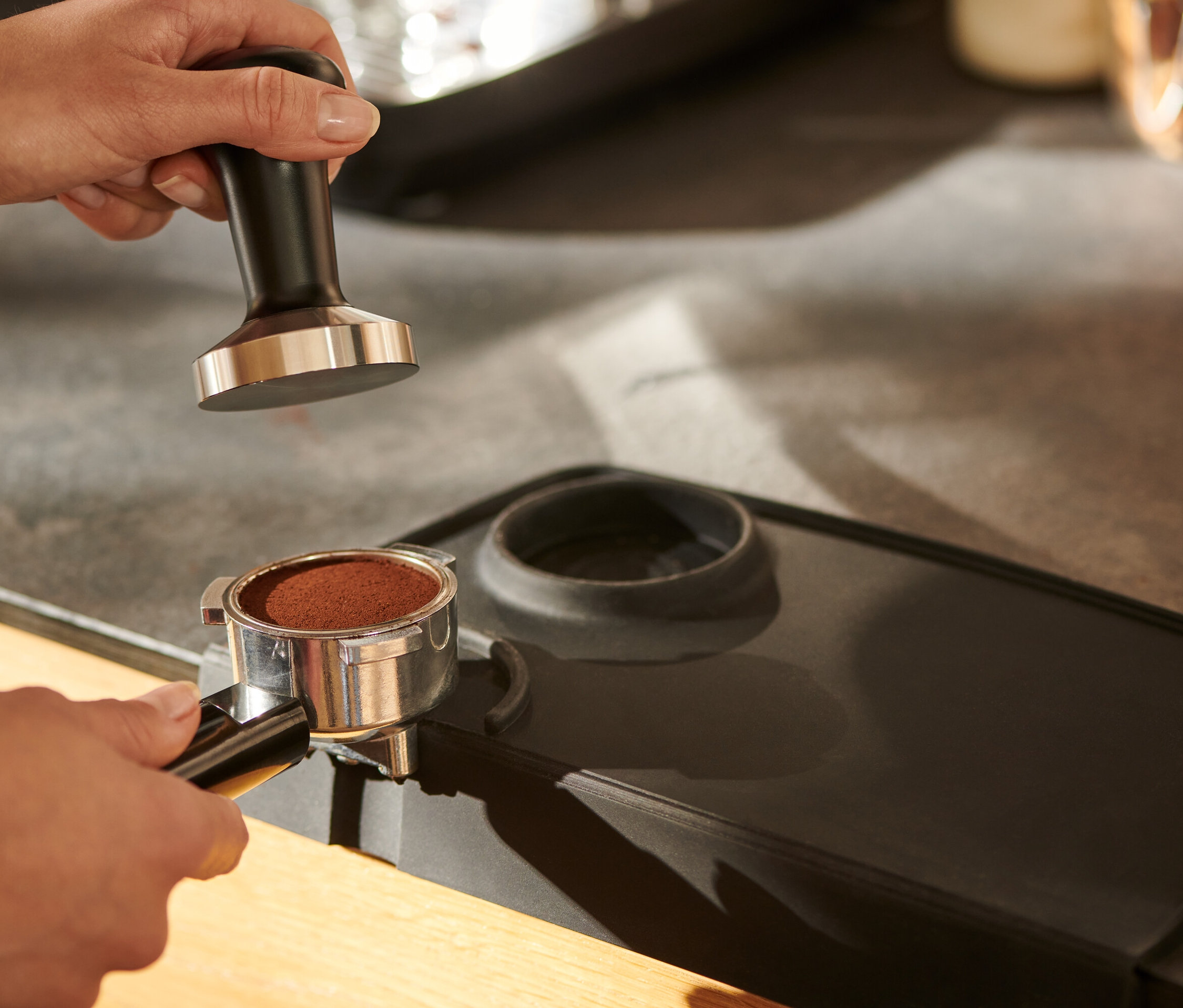 Ruka drží pěchovadlo na kávu, černé, nad podložkou na pěchování kávy.