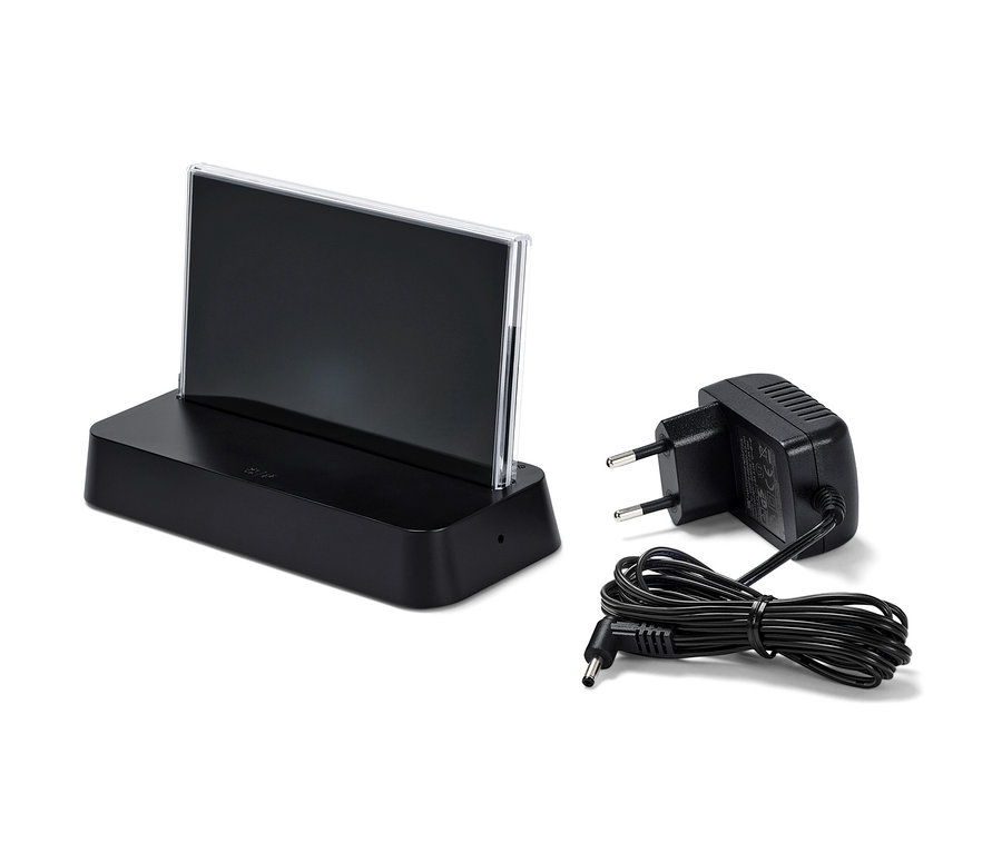 Černá meteostanice s barevným LCD displejem, řízená rádiovým signálem a napájecí adaptér na bílém pozadí.