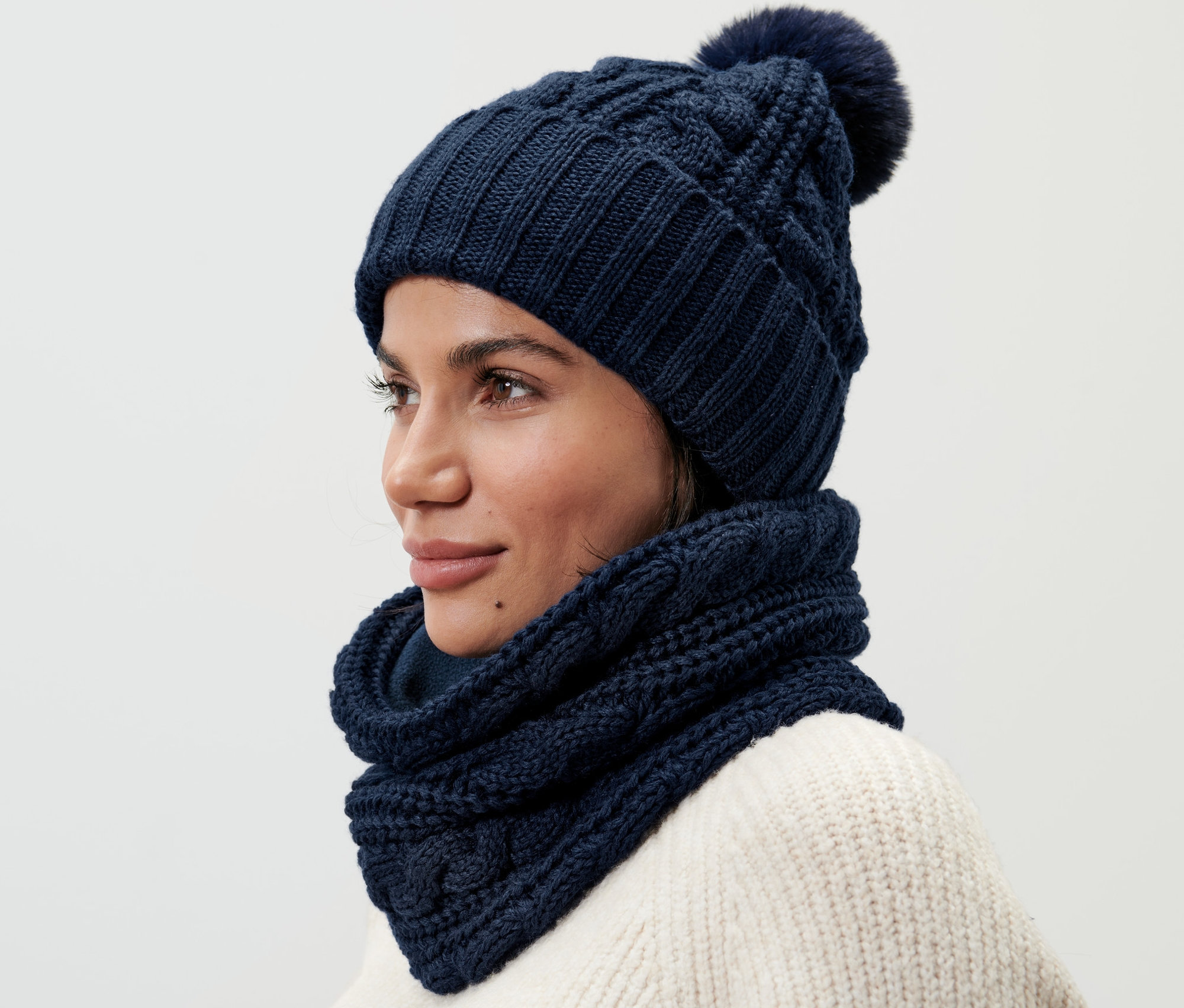 Žena má na sobě pletenou kruhovou šálu a odpovídající pletenou čepici s bambulí.