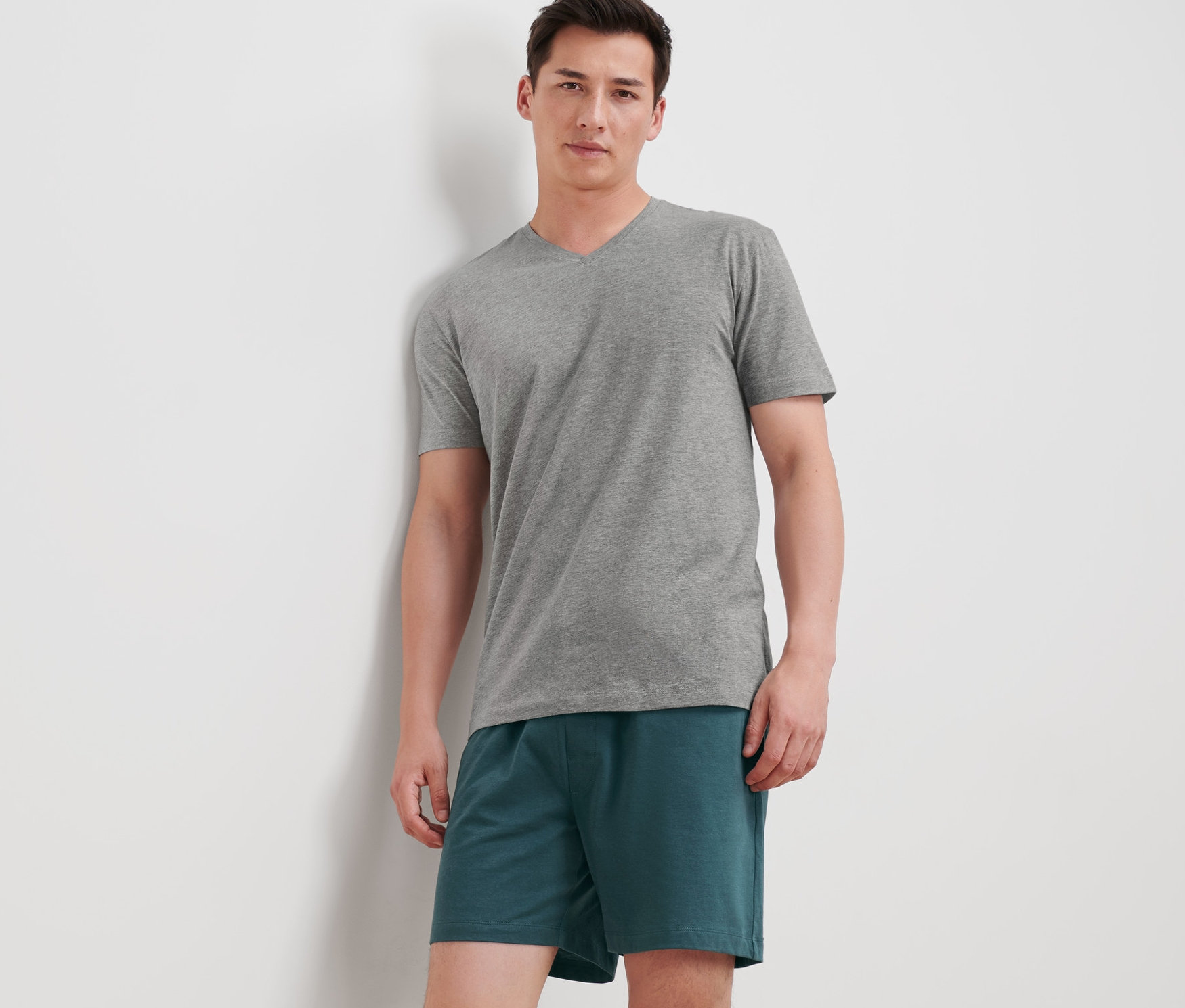 Muž opřený o zeď má na sobě krátké pyžamo.