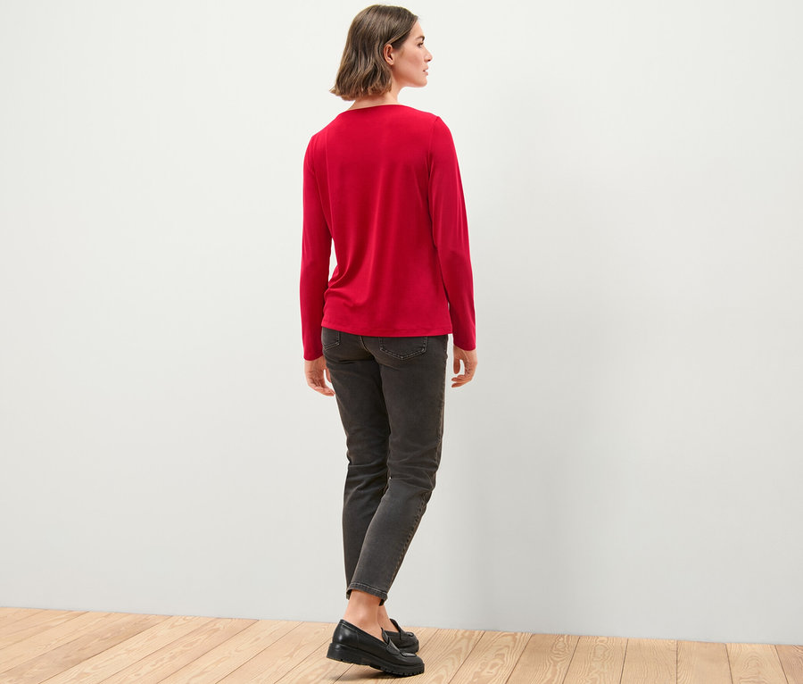 Žena stojí zády a má na sobě halenkové triko s řasením, džíny a boty.