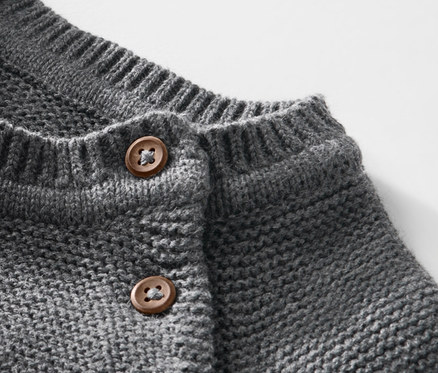 Detail dětského pleteného svetru s hnědými knoflíky.
