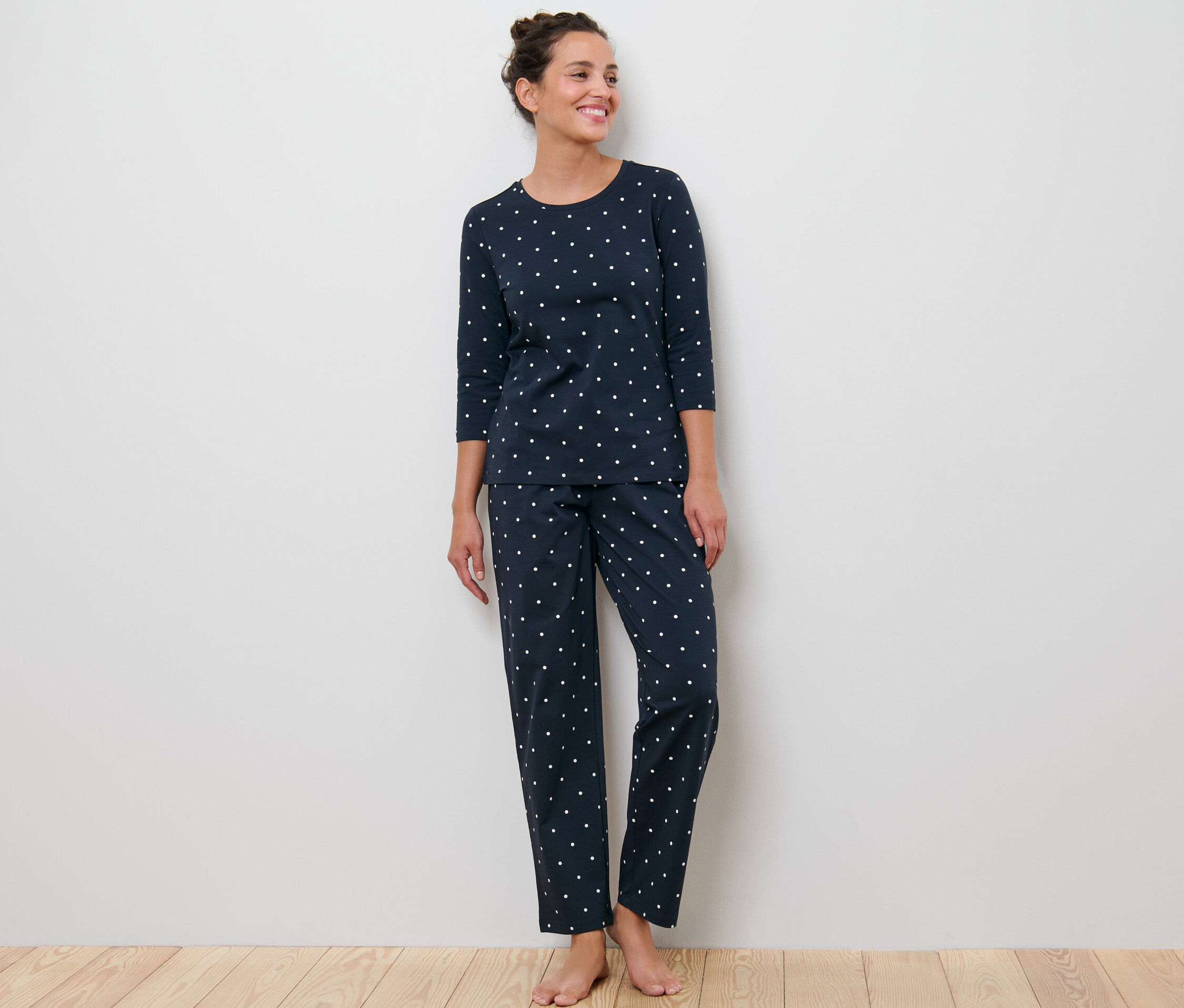 Žena stojí a má na sobě tmavě modré pyžamo s puntíky.