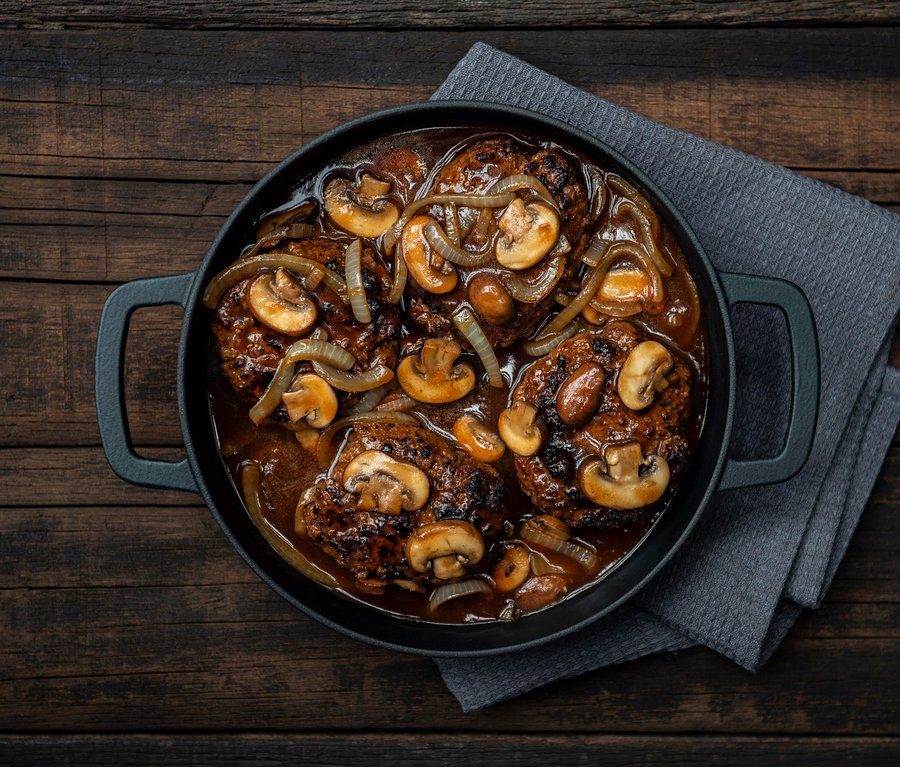 Litinová servírovací pánev »COMBEKK Sous-Chef« s masovými plátky, houbami a cibulí v omáčce.