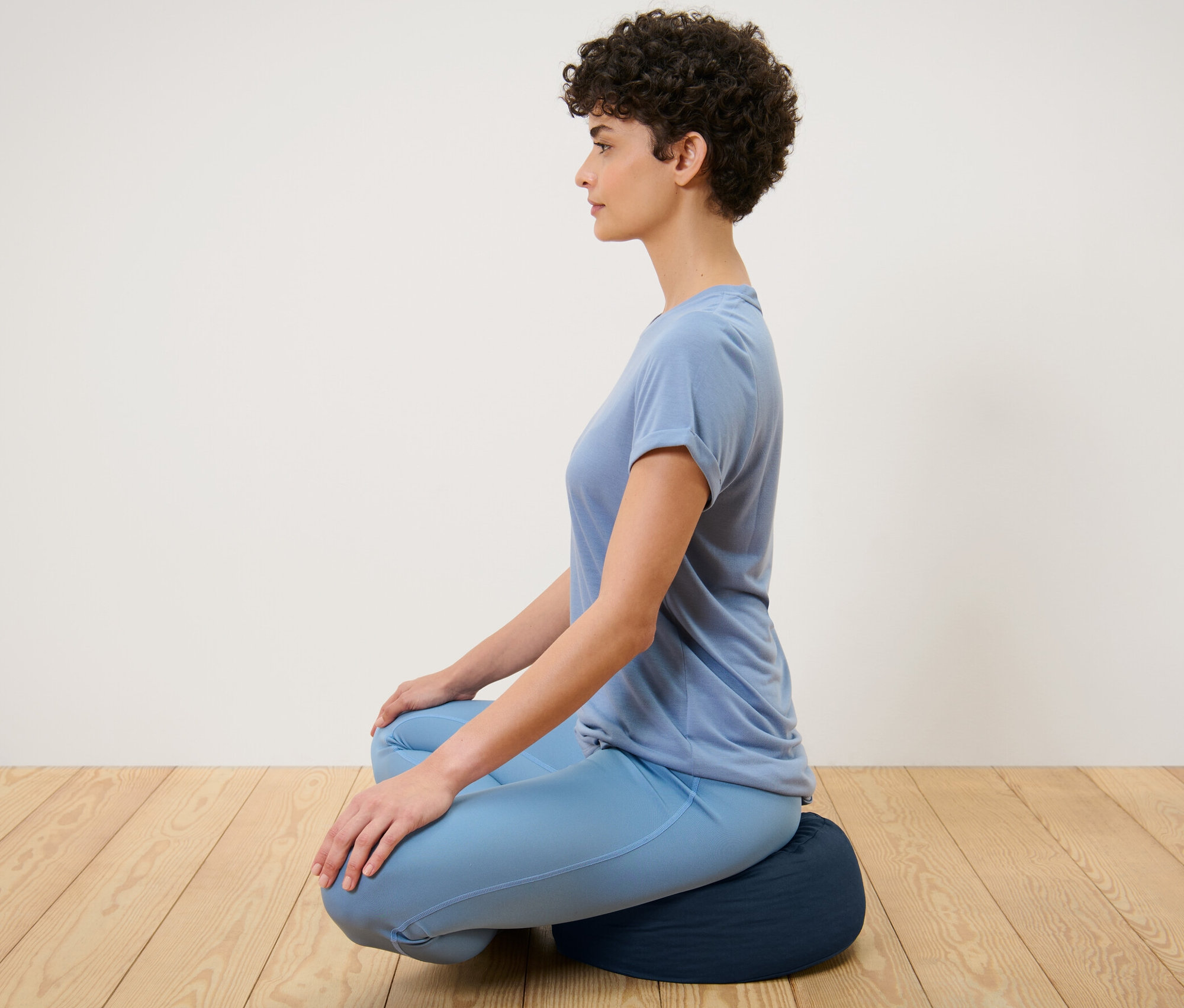 Žena sedí na meditačním polštáři.