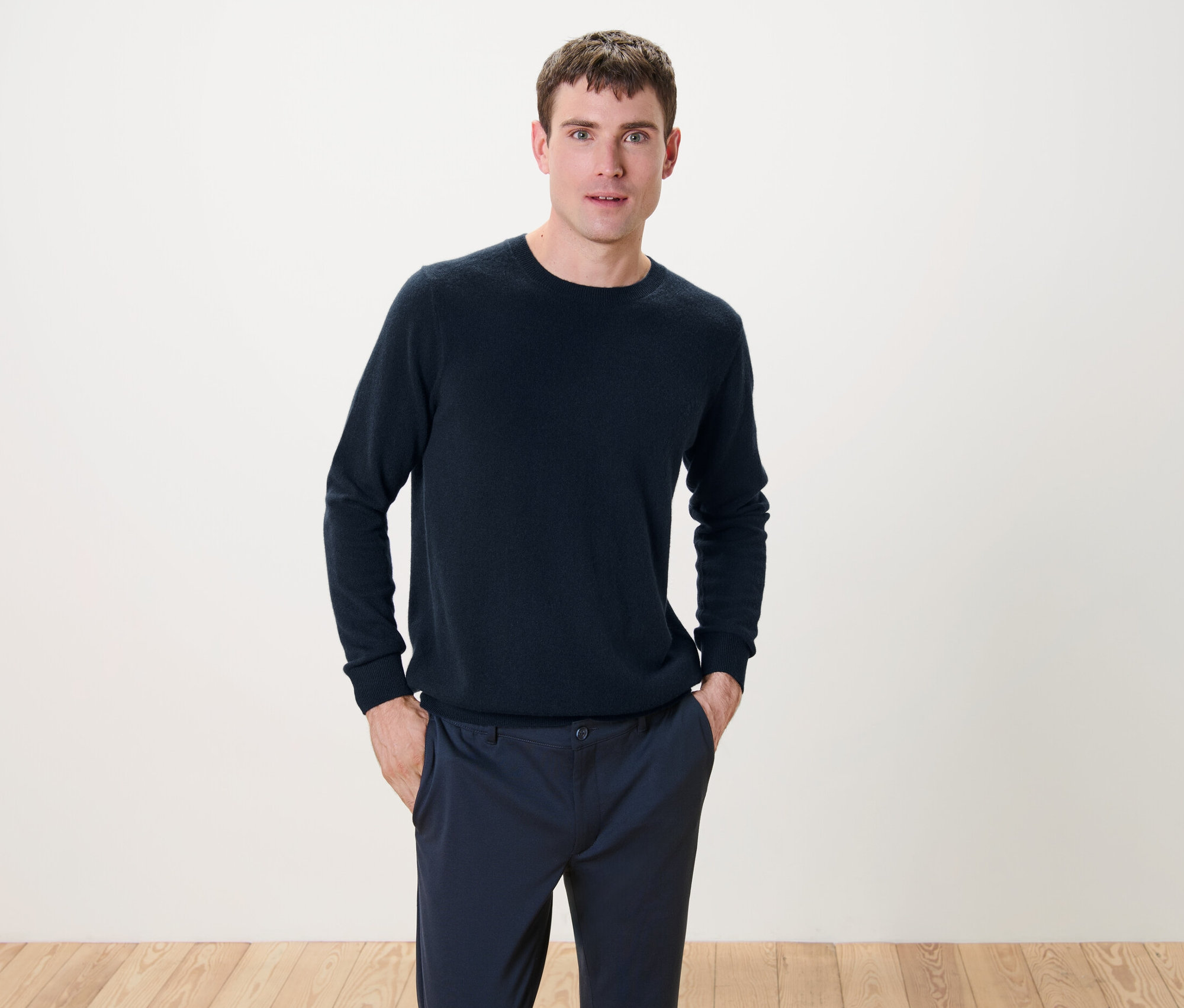 Muž stojí a má ruce v kapsách. Oblečený má kašmírový svetr s kulatým výstřihem v námořnické modré barvě.
