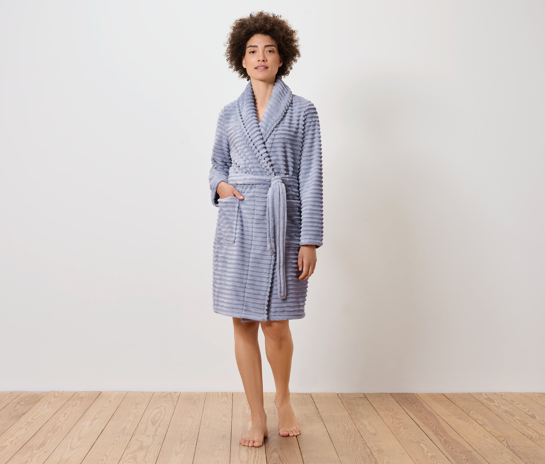 Žena stojí na dřevěné podlaze a má na sobě modrý župan.