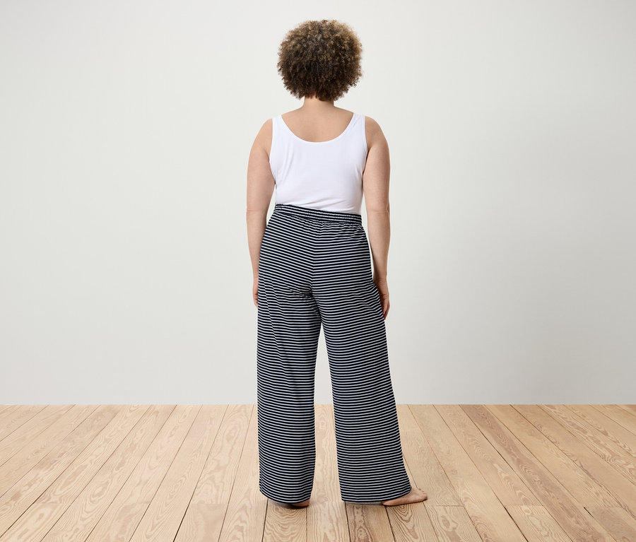Zezadu pohled na ženu s kudrnatými vlasy v bílém tílku a pruhovaných kalhotách.