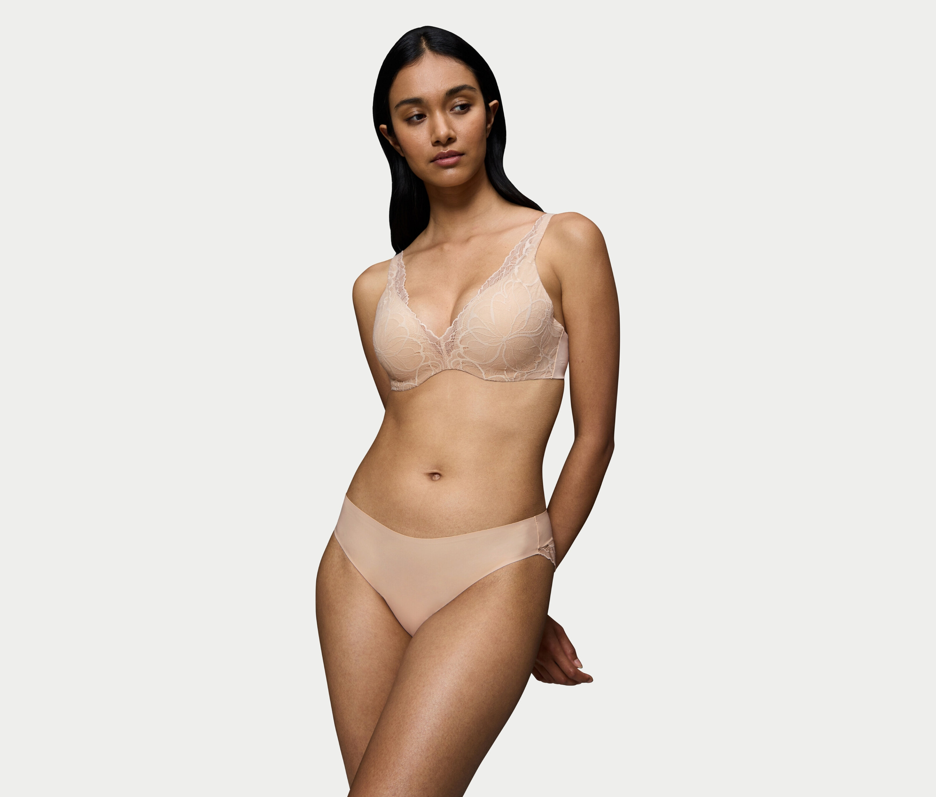 Žena pózuje v béžové krajkové podprsence a kalhotkách.