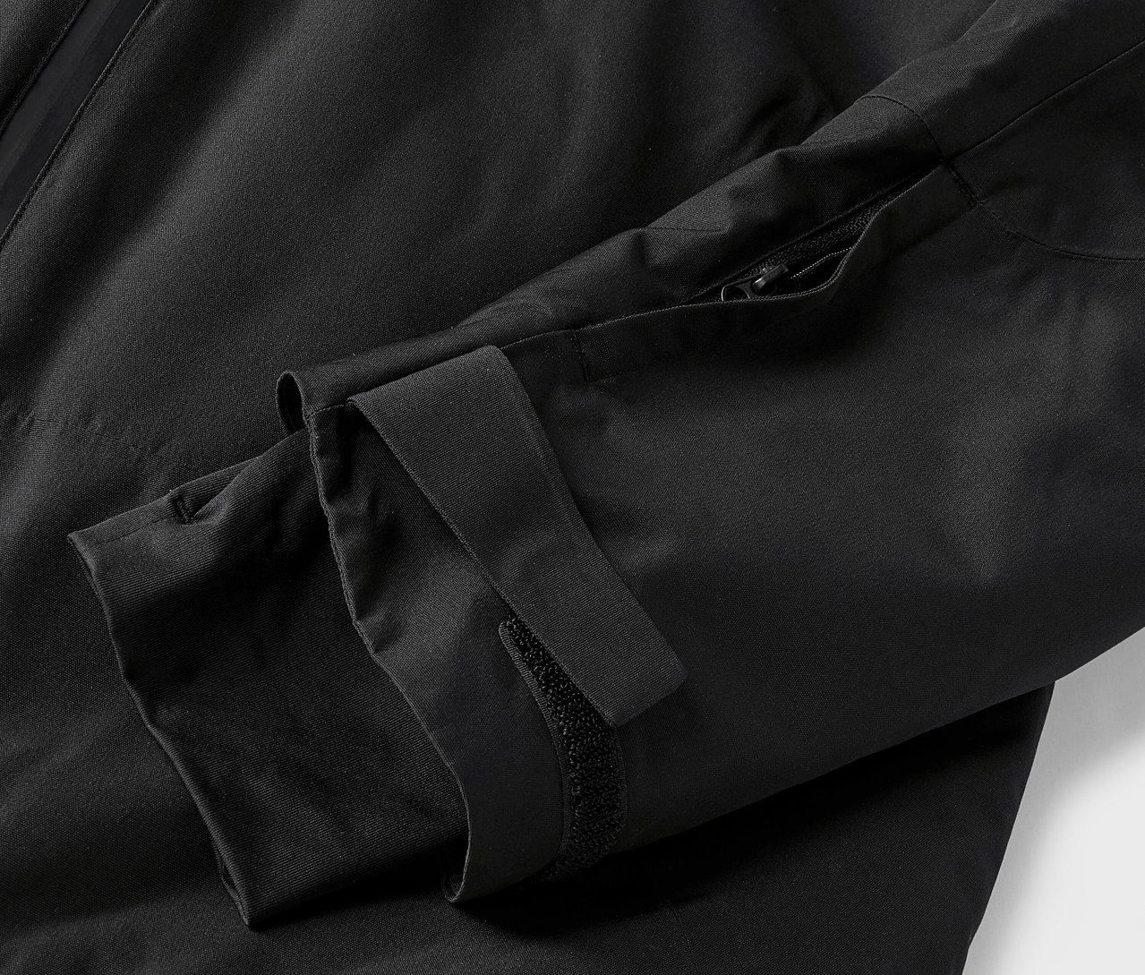 Detail černé bundy s rukávem a zipem.