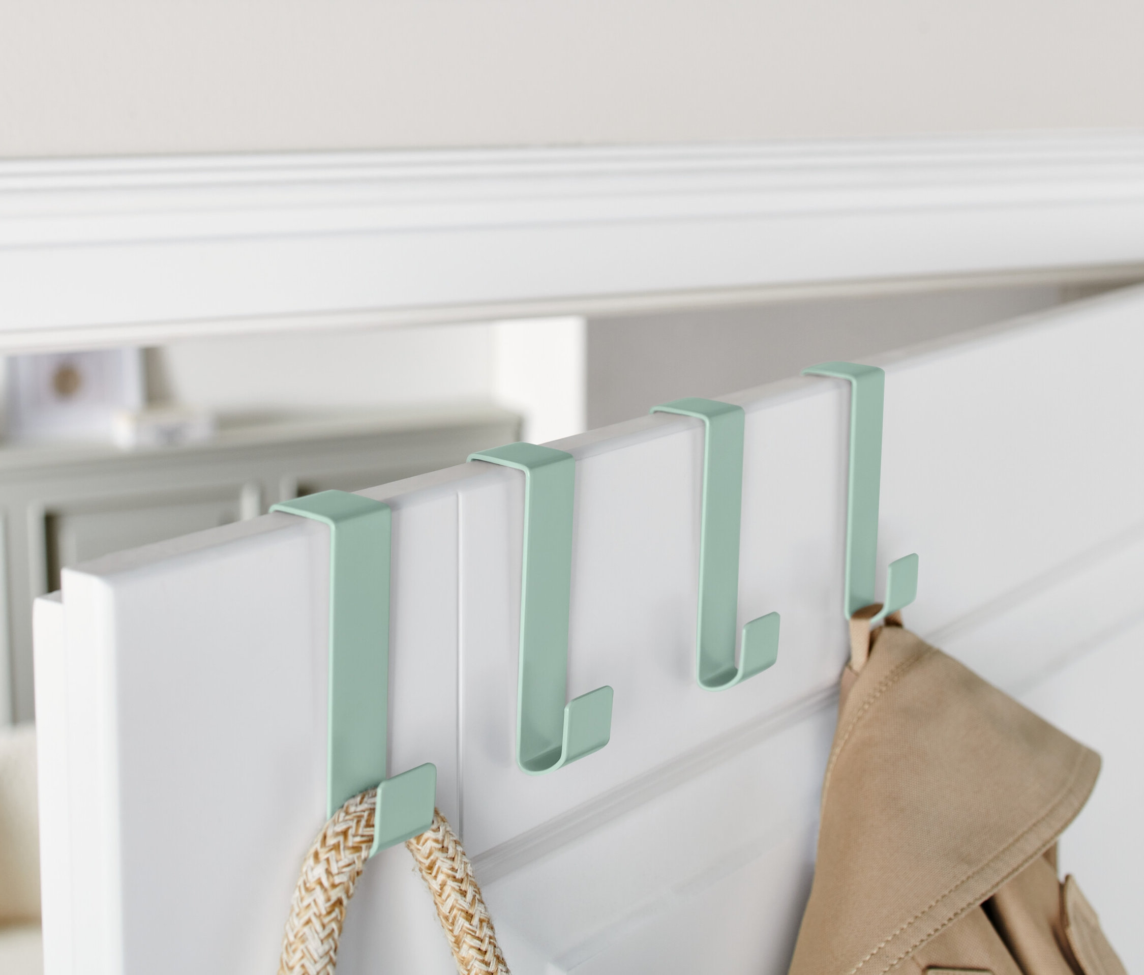 Čtyři zelené háčky na dveře visí na horní hraně bílých dveří.