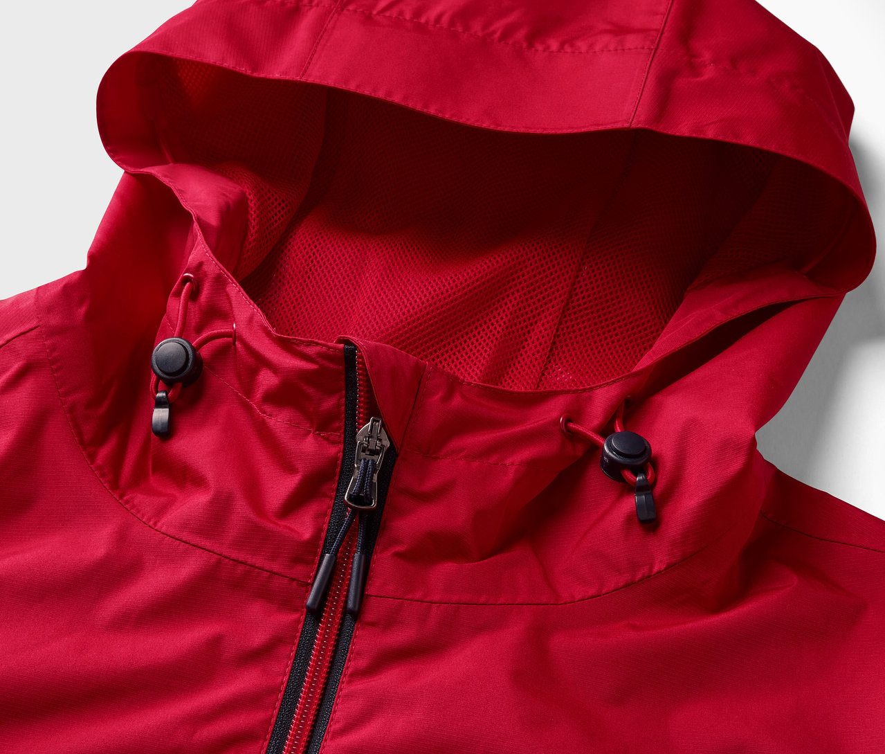 Detail červené bundy do deště se zipem a kapucí.