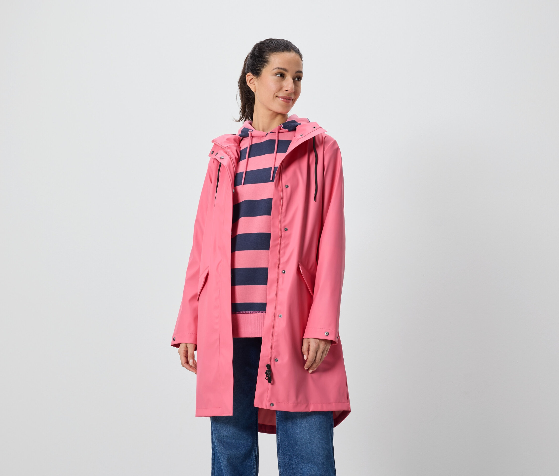 Žena má na sobě růžový kabát a pruhovanou mikinu s kapucí.