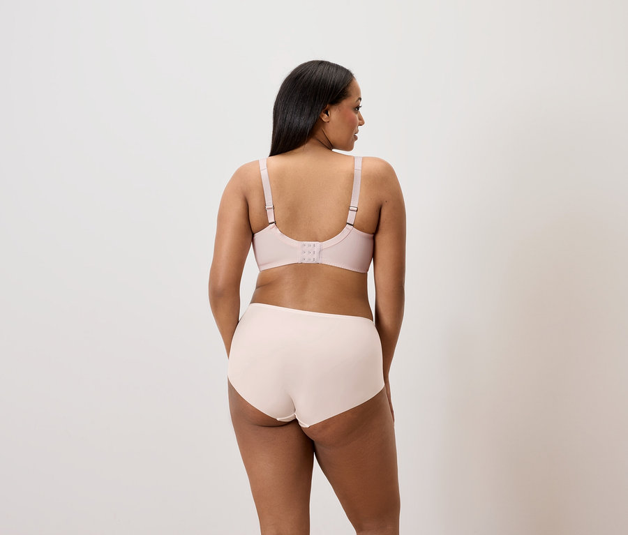 Zezadu: žena s tmavými vlasy má na sobě světle růžovou podprsenku a kalhotky.