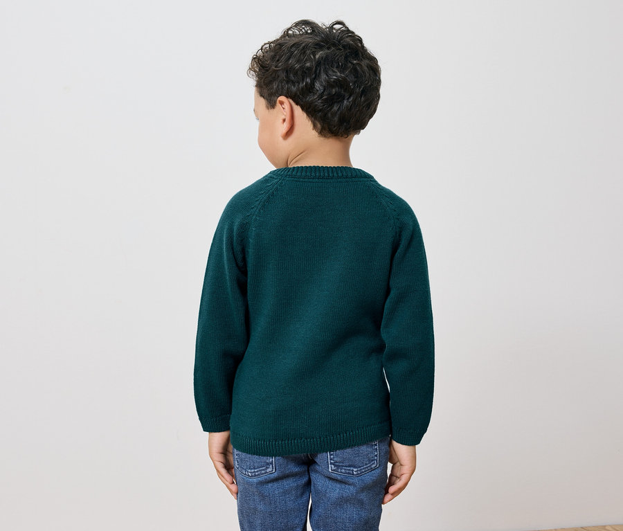 Chlapec v zeleném svetru a džínách stojí zády k fotoaparátu.