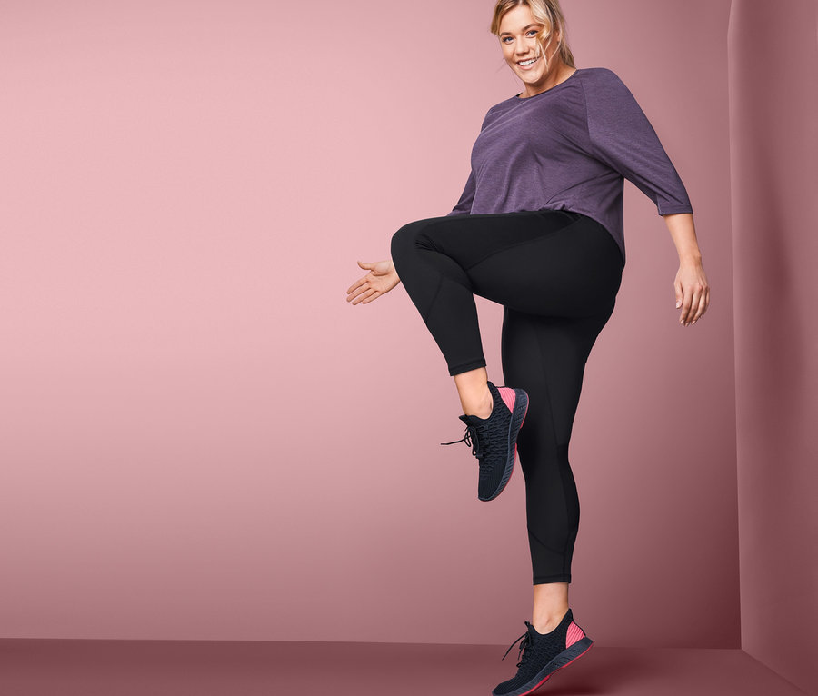 Žena pózuje ve sportovních legínách a sportovní obuvi.