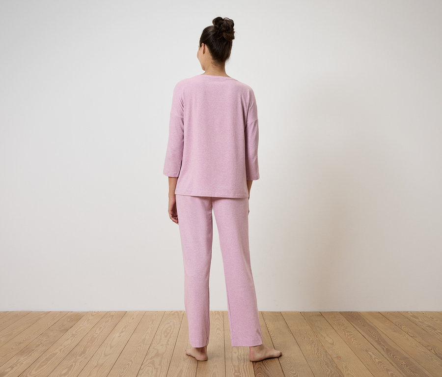 Žena stojí zády k fotoaparátu a má na sobě růžové pyžamo.