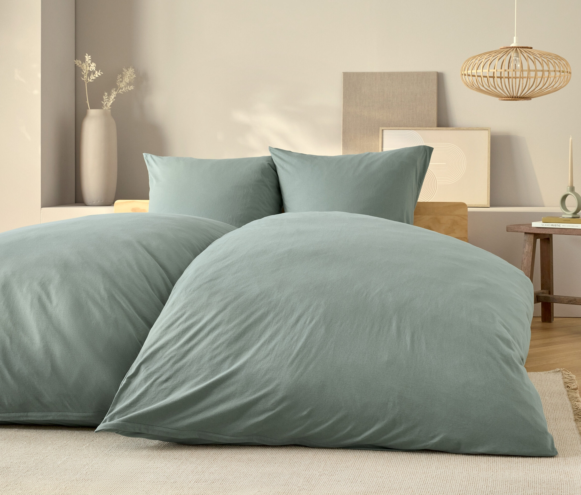 Světle modré ložní prádlo na posteli s dvěma polštáři a dřevěným nočním stolkem.