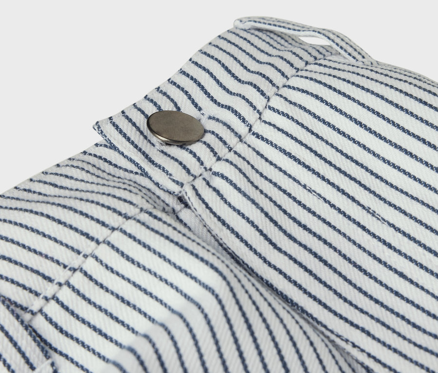 Detail dětských tkaných kalhot s modrými proužky a knoflíkem.