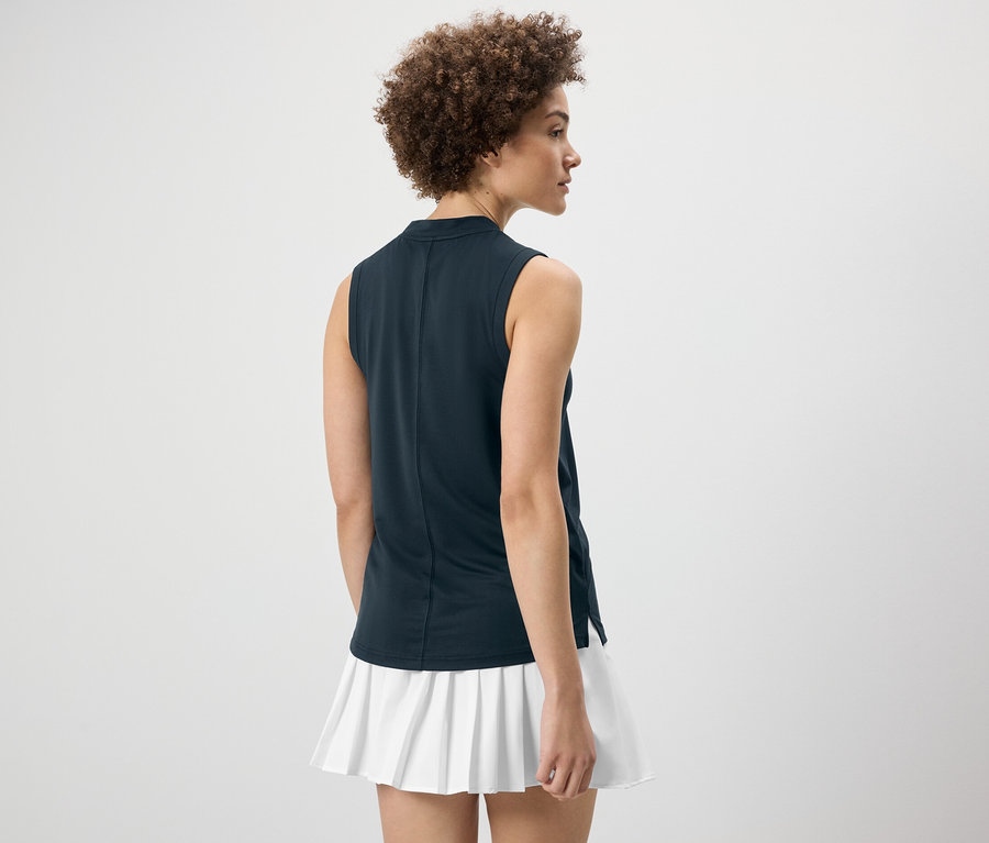 Žena zády k fotoaparátu má na sobě tmavě modrý funkční top a bílou sukni.